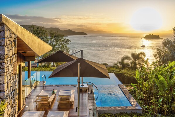 A pool area with lounge chairs and umbrellas, overlooking a body of water with distant islands.