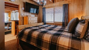 Un dormitorio acogedor con una cama grande, un televisor en la pared y una ventana con cortinas.