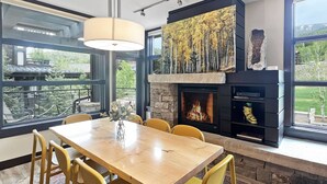 A dining area with a wooden table and yellow chairs, a fireplace, and a view of the outdoors. - Best Location in Snowmass Village! With A/C, Amazing Views, Balcony, W/D, Gas FP & Shared HT (Snowmass Village)