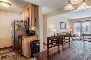 A kitchen with wooden cabinets, a refrigerator, microwave, and a dining area with a table and chairs.