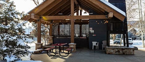 A covered outdoor area with a wooden structure, picnic tables, and a stone bench.