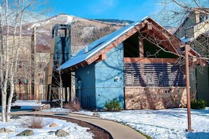 A building with a sloped roof, a stone wall, and a metal structure to the left.