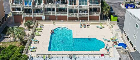 A multi-story hotel with a pool area, including lounge chairs and a children's play area.