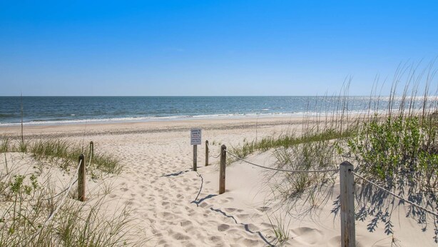 A sandy beach path leading to the ocean with a sign warning to leave it as it is.