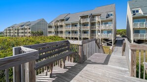 A wooden boardwalk leading to a beachfront hotel with multiple balconies and a clear view of the ocean.
