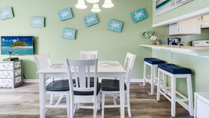 A dining area with a white table and chairs, a kitchen counter, and wall-mounted artwork.