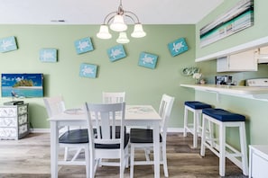 A dining area with a white table and chairs, a kitchen counter, and wall-mounted artwork.