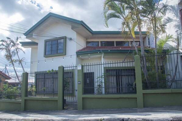 A two-story house with a green and white exterior, a red roof, and a gated entrance. - Las Carmelas, Airport Juan Santamaría, Alajuela, San José (Alajuela)