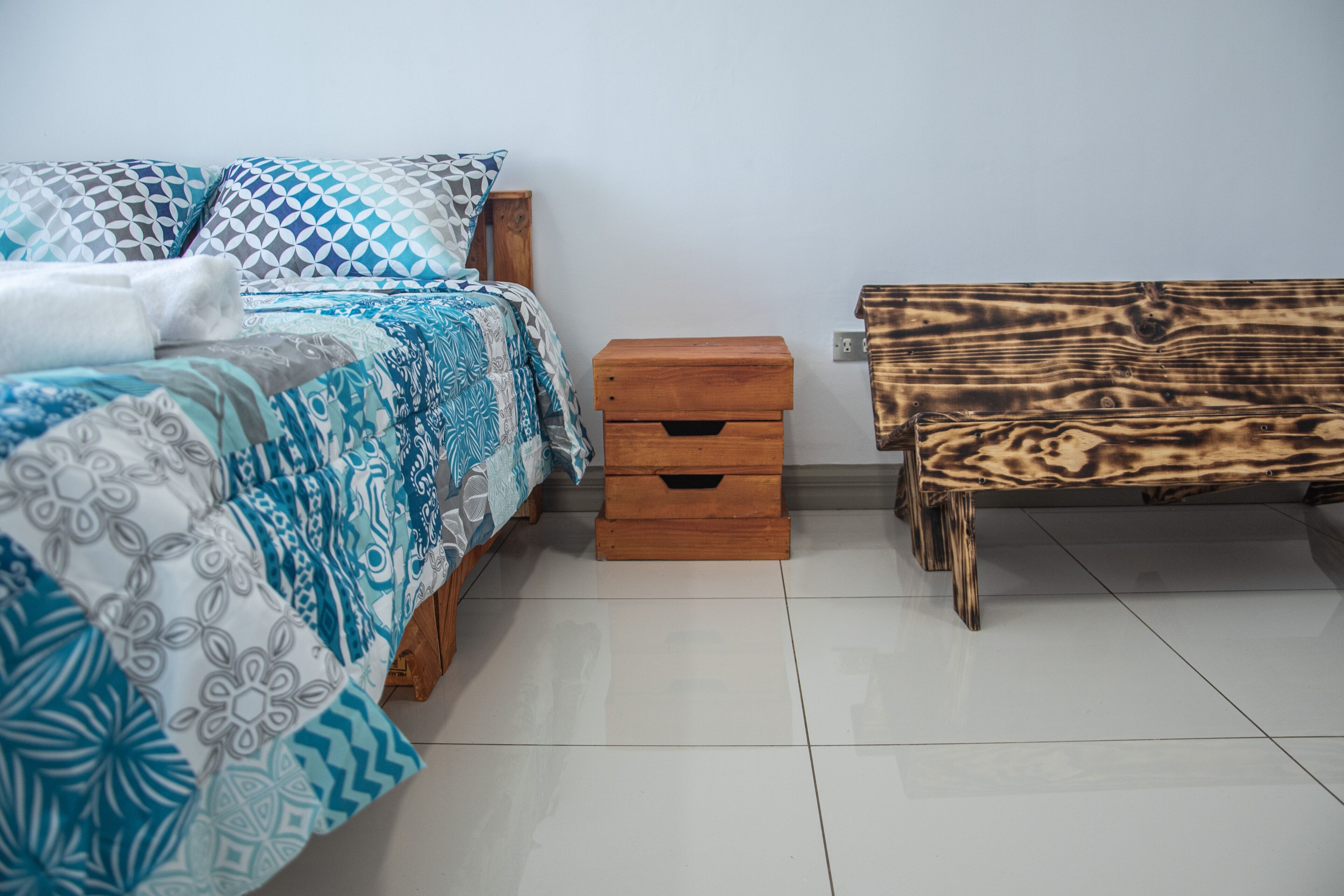 Een slaapkamer met een bed, een nachtkastje van hout met lades en een bankje.