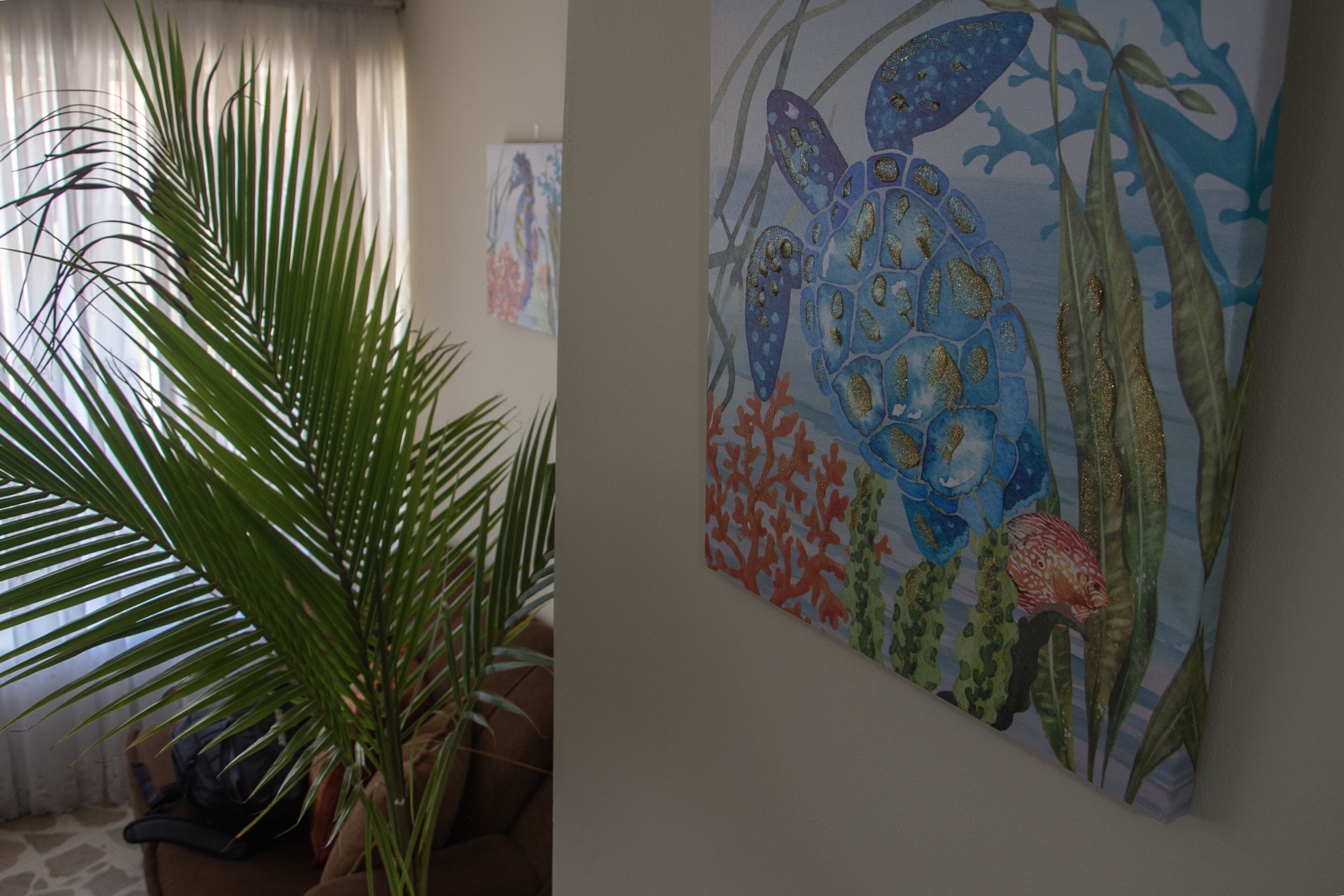 Um quarto com uma grande planta em vaso, uma parede com uma pintura colorida e uma janela com cortinas.