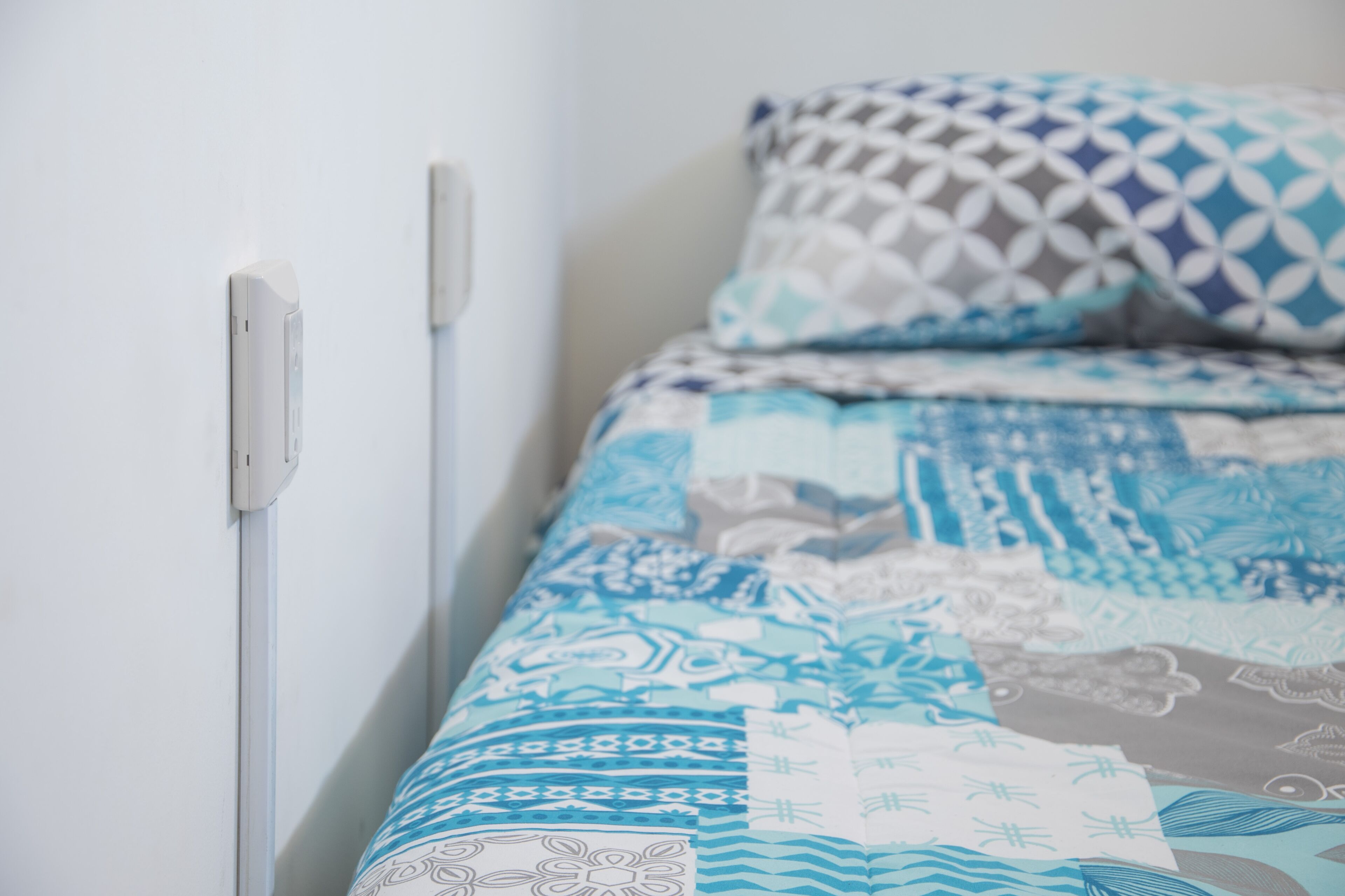 Una cama con ropa de cama estampada y una pared blanca con un enchufe.