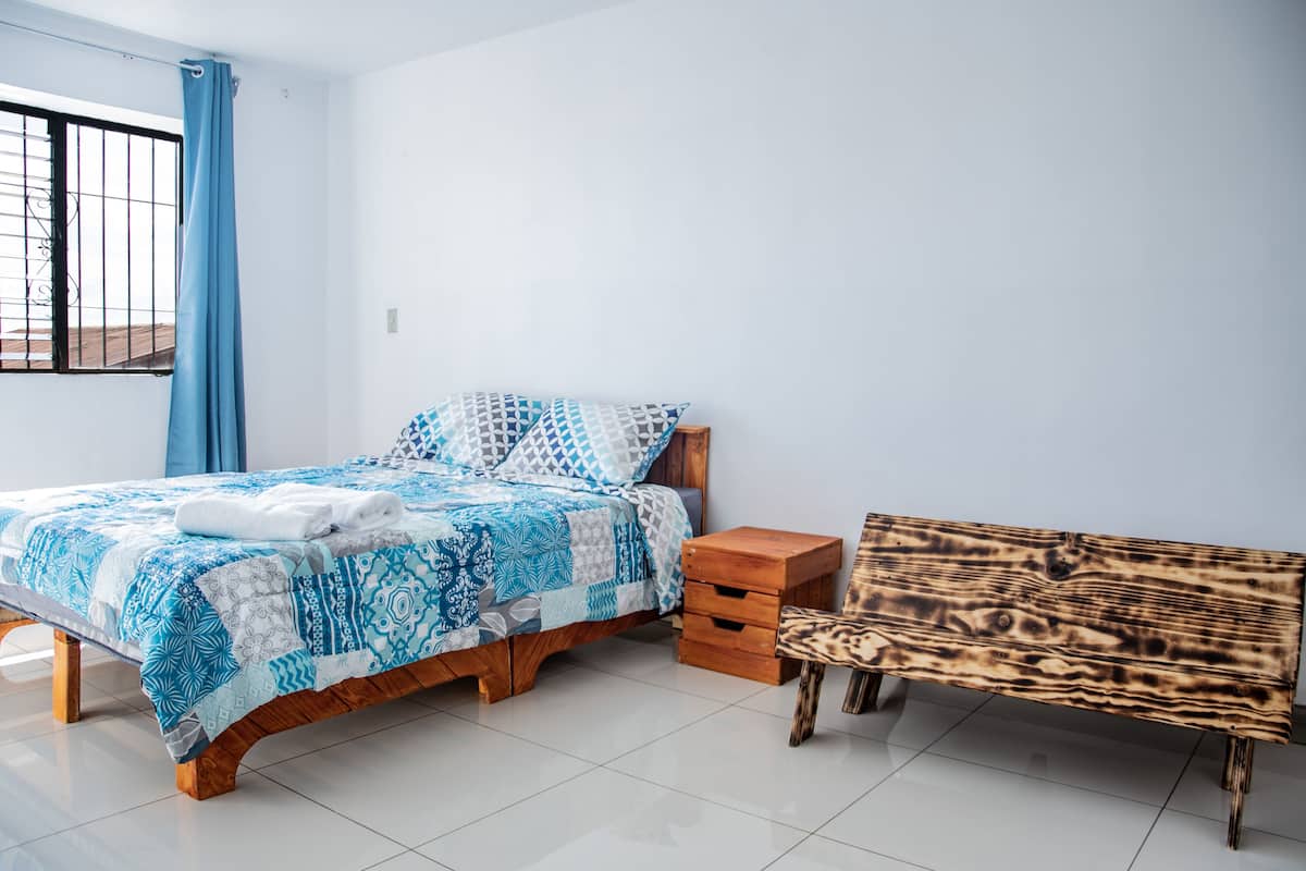 A bedroom with a bed, a wooden bench, and a window with a curtain.