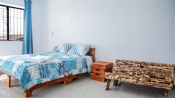 A bedroom with a bed, a wooden bench, and a window with a curtain.