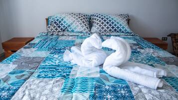 Una cama con una colcha azul y blanca estampada, dos almohadas con diseños geométricos y dos toallas blancas dispuestas en forma de cisne.