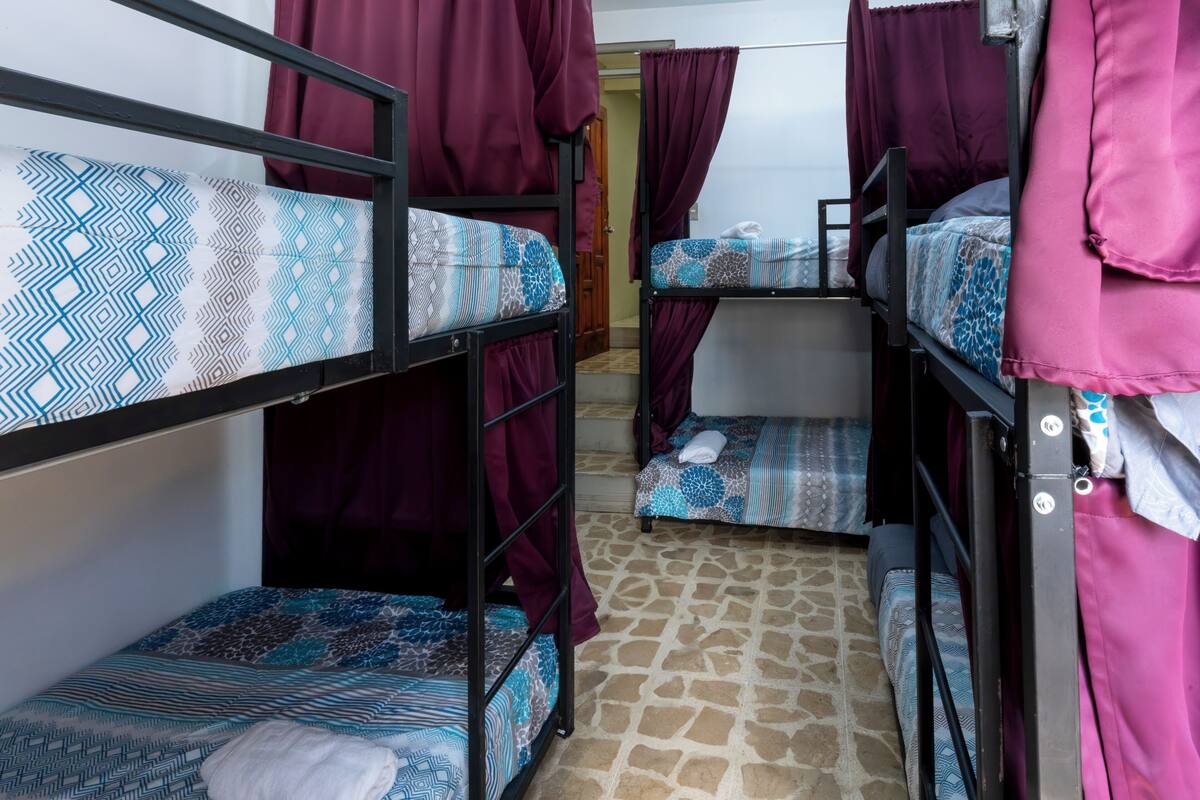 A dormitory room with bunk beds, patterned bedding, and curtains.