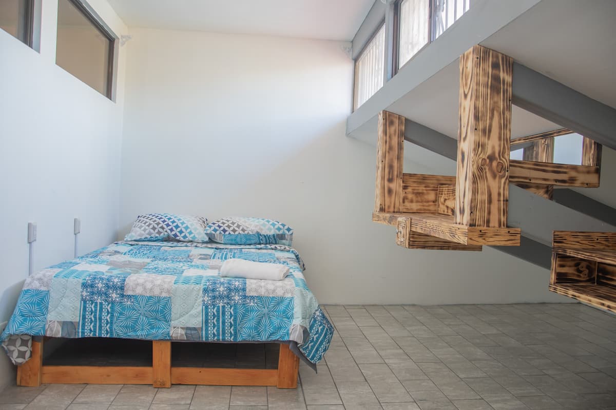 A bedroom with a wooden bed frame, a blue and white quilt, and a slanted ceiling with wooden beams.