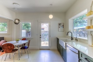 A modern kitchen with a dining area, white cabinetry, and a view through the door. - Cute remodeled bungalow near UA (Tucson)