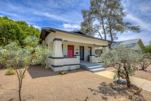 A single-story house with a red door, a covered porch, and a small front yard with desert landscaping. - Cute remodeled bungalow near UA (Tucson)