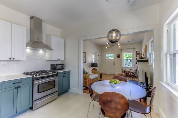 A modern kitchen with a gas stove, oven, and microwave. There is a dining area with a round table and chairs.