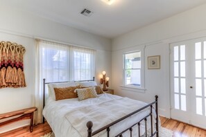 A bedroom with a bed, wooden floor, white walls, a window, and a door. - Cute remodeled bungalow near UA (Tucson)