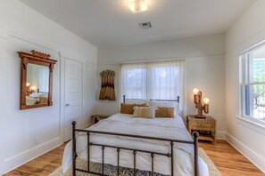 A bedroom with a bed, bedside tables, a mirror, and a window.