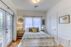 A bedroom with a bed, bedside table, lamp, and a window with curtains. - Cute remodeled bungalow near UA (Tucson)