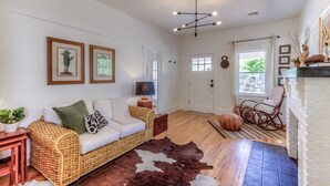 A living room with a wicker sofa, a cowhide rug, a fireplace, and framed artwork on the wall.