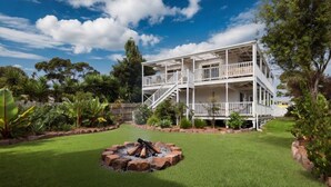 A two-story building with a balcony, surrounded by a well-maintained lawn and various plants. - Renovated open planned living sun drenched house in Cape Woolamai (Cape Woolamai)
