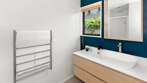 A modern bathroom with a white sink, a large mirror, and a towel rack.