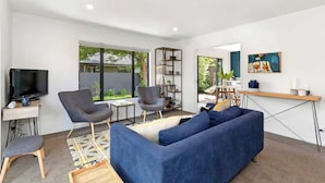 A modern living room with a sofa, chairs, a TV, a bookshelf, and a dining area.