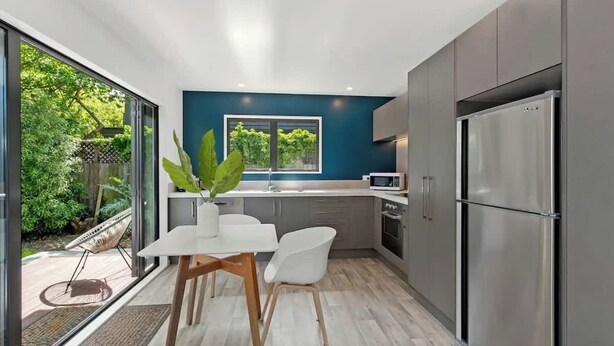 A modern kitchen with a large window, stainless steel appliances, and a dining area with a white table and chairs.