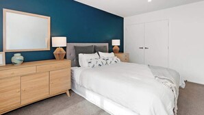 A bedroom with a bed, bedside tables, a dresser, a mirror, and a door.