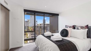 A modern bedroom with a large bed, a view of the city through a sliding door, and a balcony. - Latimer View Apartment (Christchurch)