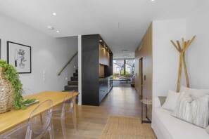 Un interior moderno con una mesa de comedor de madera, sillas traslúcidas, un sofá y una escalera.