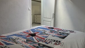 Une chambre à coucher avec un lit recouvert d’une couette aux motifs du drapeau britannique, une porte et un couloir menant à une autre pièce.