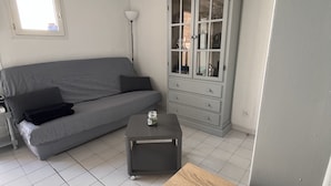 Um quarto com sofá cinzento, mesa de madeira, aparador com portas de vidro e abajur.