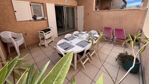 Um pátio com uma mesa e cadeiras, uma planta em vaso e uma porta de correr.