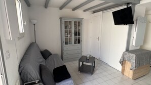 Quarto com sofá cinza, uma mesinha, armário, cama e televisão fixada na parede.
