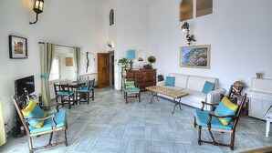 Een ruime woonkamer met een grote spiegel, een eethoek met houten stoelen, een bank en een salontafel.