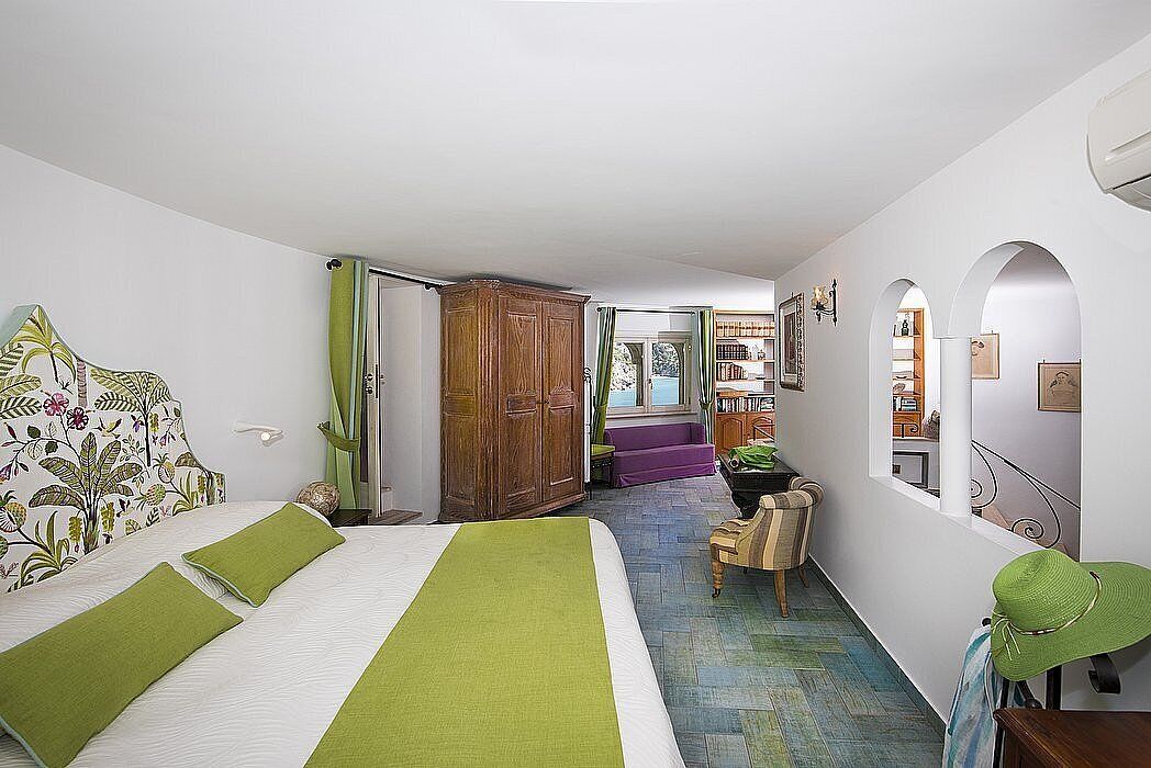 A bedroom with a bed, a wooden wardrobe, a chair, and a window.