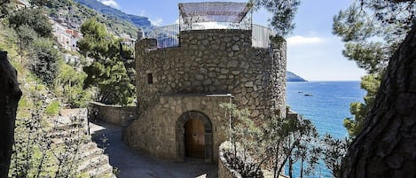 A stone building with a wooden door, a balcony, and a view of the sea.