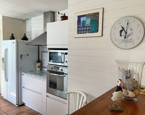 A kitchen with a microwave, oven, and refrigerator. There's a clock on the wall and a decorative bird on the table.