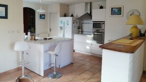 Une cuisine moderne avec des meubles blancs, un îlot central doté de tabourets de bar, un four à micro-ondes, un four traditionnel et une lampe jaune posée sur le plan de travail.
