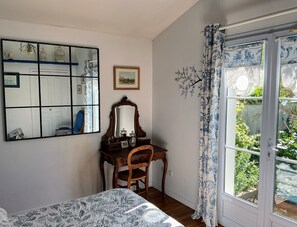 A bedroom with a bed, a desk with a mirror, a picture on the wall, and a window with curtains.