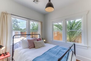 A bedroom with a bed, a bedside table with a lamp, and a window with a view of palm trees. - Remodeled Gem 5 minutes to UA (Tucson)