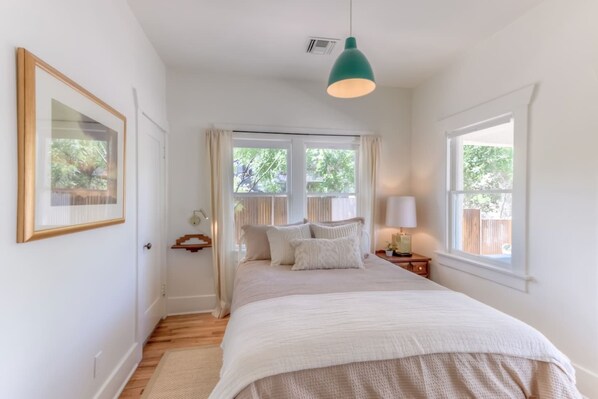 A bedroom with a bed, bedside tables, a hanging light fixture, and windows. - Remodeled Gem 5 minutes to UA (Tucson)