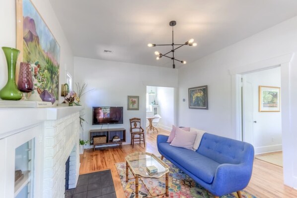 A living room with a fireplace, a blue sofa, a television, and a chandelier. - Remodeled Gem 5 minutes to UA (Tucson)
