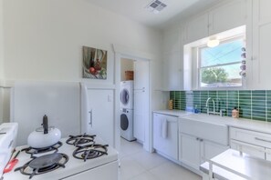 A modern kitchen with white cabinetry, a gas stove, a washing machine, and a window with a view.