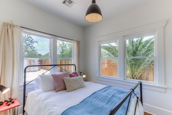 A bedroom with a bed, bedside table, lamp, and large windows with views of greenery.