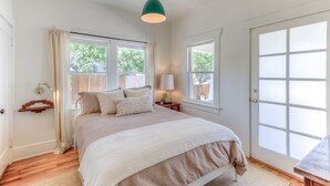Un dormitorio con cama, ventana, puerta y lámpara colgante.